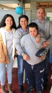 The Rodert Family on a sofa, The four of them look happy and James is wearing a blue top being held by his parents